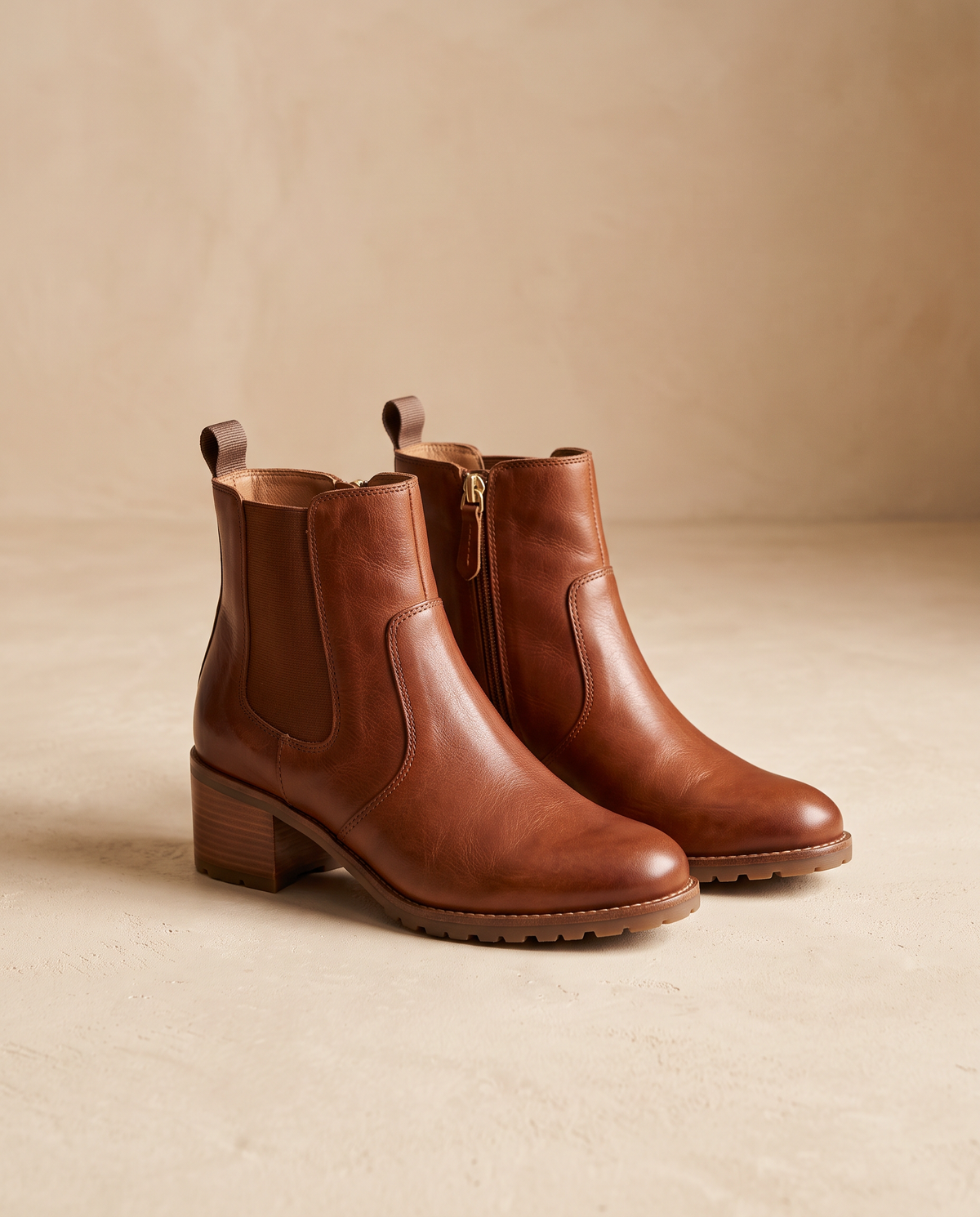 Damenschuhe – cognacfarbene Leder-Stiefeletten vor beigem Hintergrund